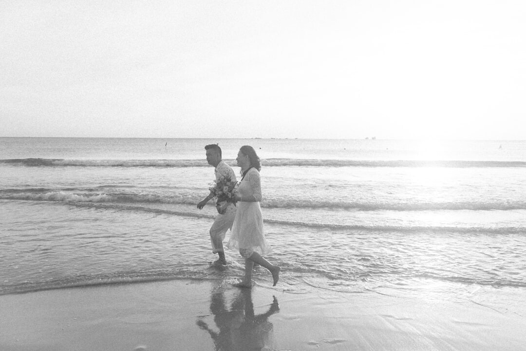 Bride and groom silhouette walking on the beach at sunset